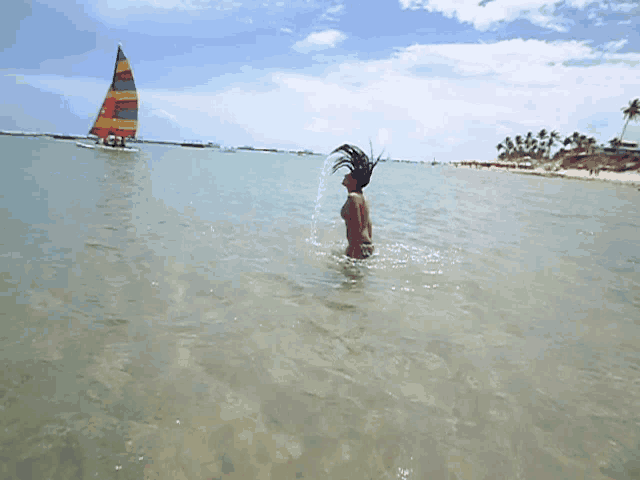 a woman is splashing her hair in the ocean with a sailboat in the background