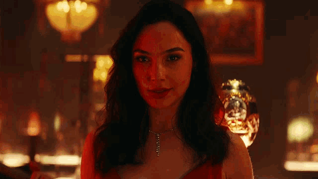 a woman is smiling in a dark room with a glass in the background