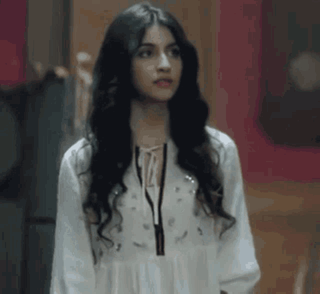 a woman with long hair is wearing a white dress and standing in front of a painting .