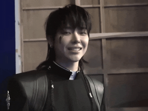 a man with a tattoo on his face is smiling and wearing a black jacket