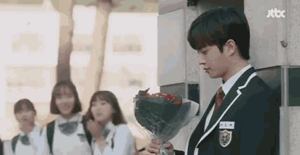 a man in a school uniform is holding a bouquet of flowers in front of a group of girls .