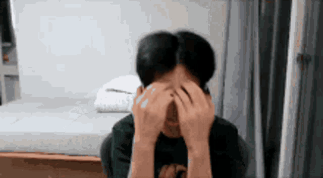 a man is covering his face with his hands while sitting in a chair