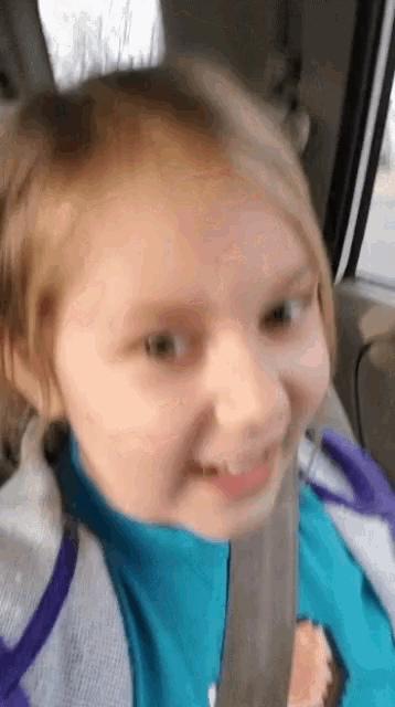 a little girl is wearing a seat belt and smiling while sitting in a car .