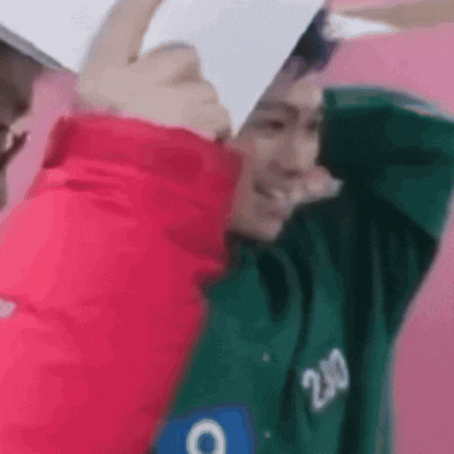 a man in a green hoodie is holding a piece of paper in his hand .