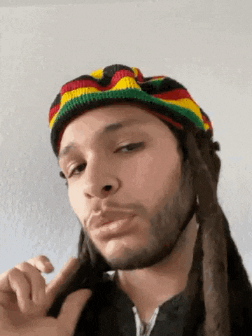a man with dreadlocks is wearing a rasta hat and making a funny face .