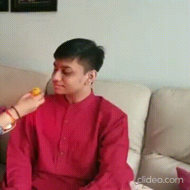 a man in a red shirt is sitting on a couch while a woman feeds him a lemon .