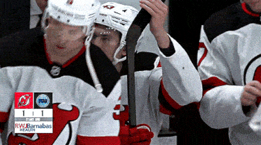 a hockey player holds a stick in front of a scoreboard that says rw barnahawas health