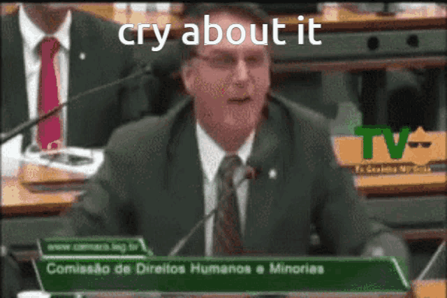 a man in a suit and tie is speaking into a microphone with the words cry about it written above him
