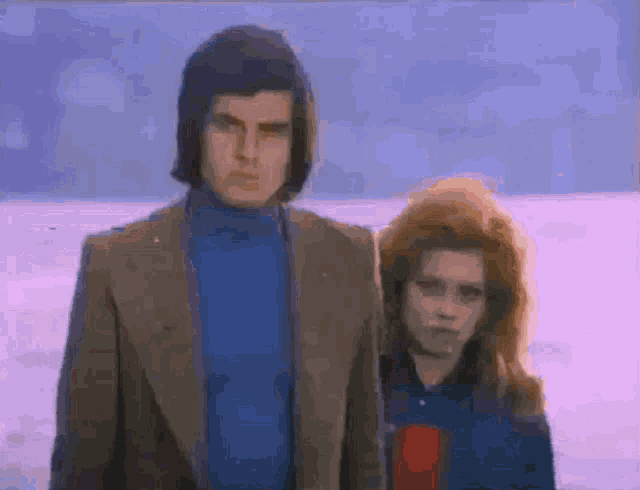a man and a woman standing next to each other in front of a snowy field