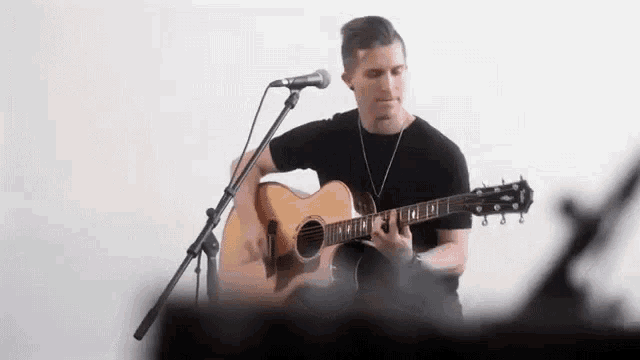 a young man is playing an acoustic guitar and singing into a microphone .
