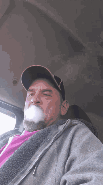 a man with a beard and hat is smoking a cigarette in a car