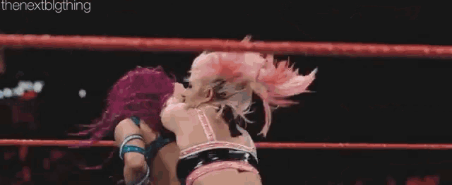 two women are wrestling in a ring and one of them is wearing pink hair .