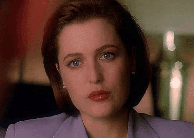 a woman with red hair and blue eyes is wearing a purple jacket