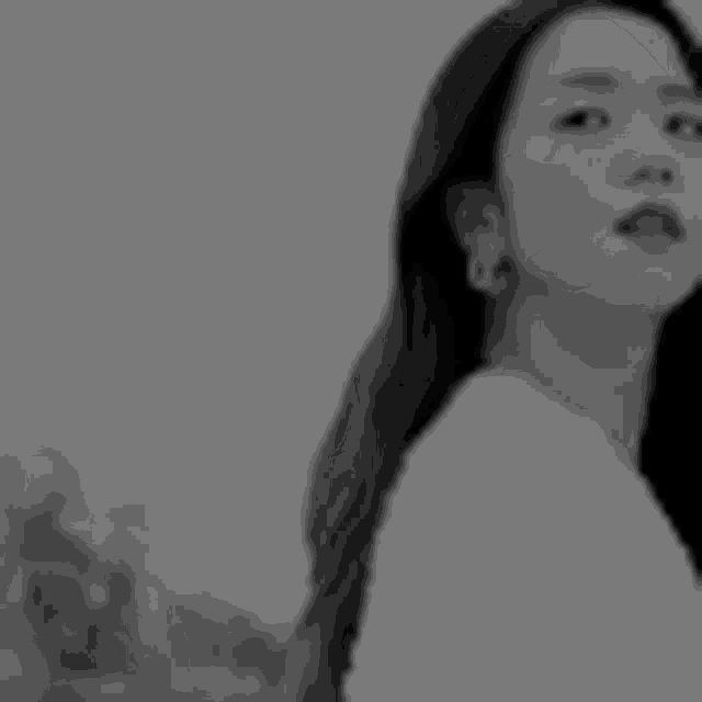 a black and white photo of a woman with long hair and earrings looking at the camera .