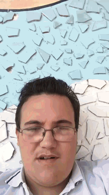a man wearing glasses and a white shirt is laying in front of a wall of broken glass