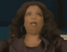 a woman with a surprised look on her face is wearing a purple shirt and earrings .