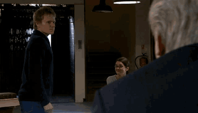 a man in a black sweater stands in front of a fire extinguisher in a dark room