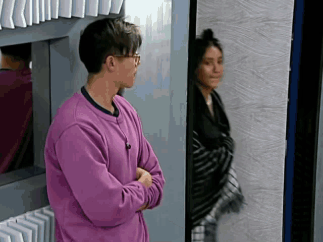 a man in a purple sweater stands in front of a mirror with his arms crossed