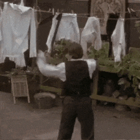 a man in overalls is standing in front of a clothes line holding a sword .