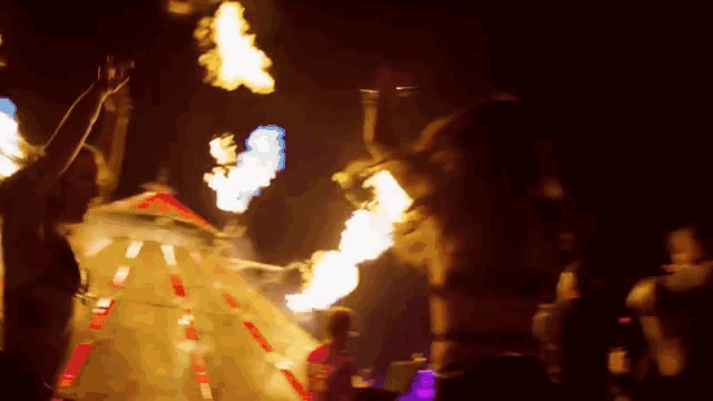 a group of people are dancing in a dark room with flames in the background