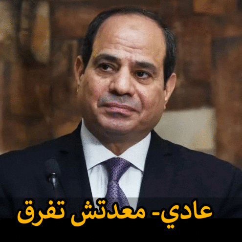 a man in a suit and tie stands in front of a microphone with arabic writing behind him