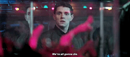 a man in a suit is standing in a dark room with a sign that says `` we 're all gonna die . ''