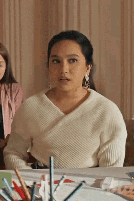 a woman wearing a white sweater and earrings is sitting at a desk
