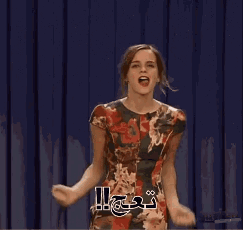 a woman in a floral dress is standing in front of a blue curtain with her arms outstretched .
