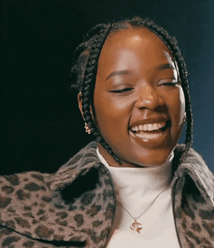 a woman wearing a leopard print jacket and a white turtleneck is smiling