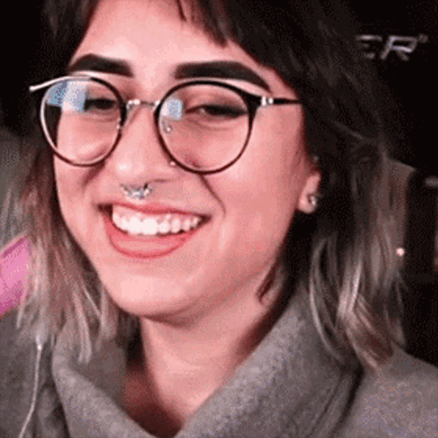 a woman wearing glasses and a nose ring smiles for the camera .