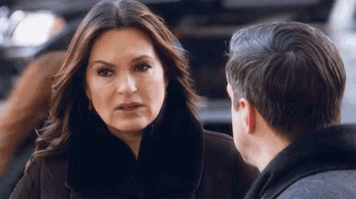 a woman in a fur coat talks to a man in a grey jacket
