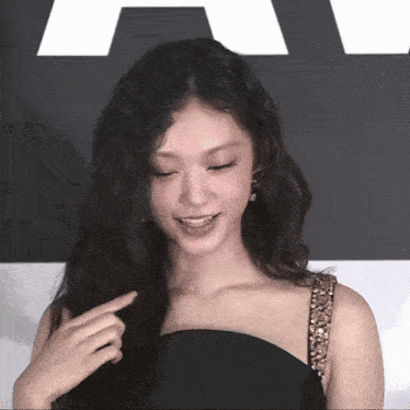a woman in a black dress is pointing at her hair and smiling