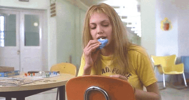 a woman wearing a yellow shirt that says air force is sitting in an orange chair eating something