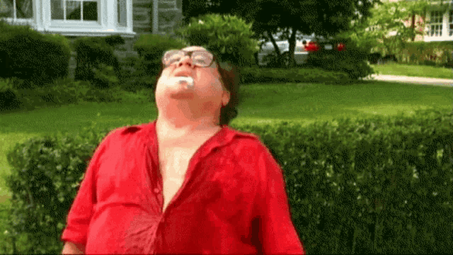 a man wearing glasses and a red shirt is standing in front of a house with his mouth open ..