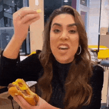 a woman is eating a hot dog in a restaurant and holding a french fry in her hand .