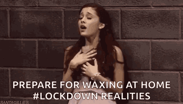 ariana grande is standing in front of a brick wall with her hands on her chest and singing .