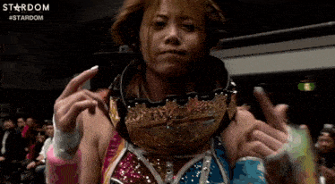 a woman in a wrestling ring is wearing a crown on her head and giving the middle finger .