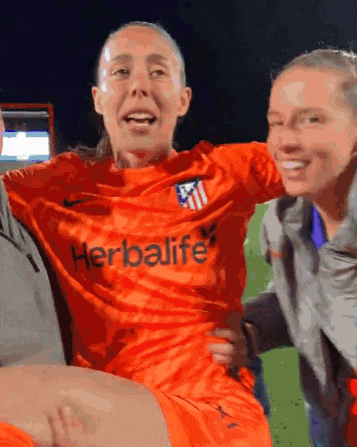 a woman in an orange herbalife shirt is being carried by two people
