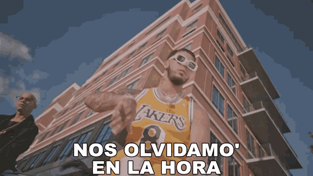 a man wearing a lakers jersey stands in front of a tall building