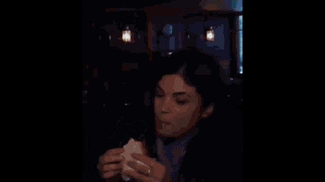 a woman is eating a hamburger in a dark room
