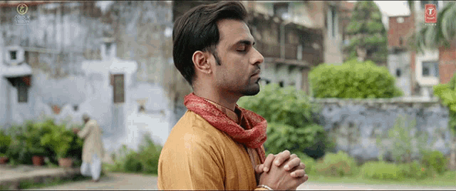 a man in a yellow shirt with a red scarf around his neck is praying with his eyes closed