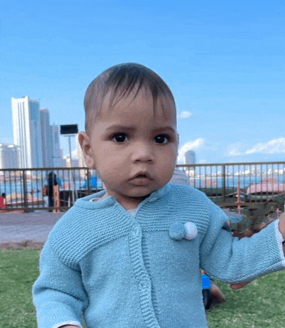 a baby is wearing a blue sweater and standing on a grassy field .