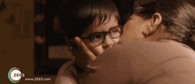 a woman kissing a child 's forehead with a zee5 logo on the bottom