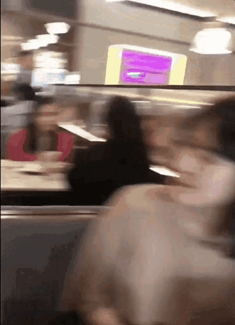 a blurry picture of people sitting in a restaurant with a purple sign in the background