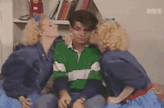 two women kissing a man on the cheek in a room .