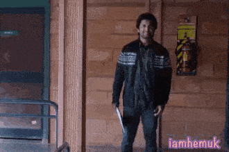 a man in a black jacket is standing in front of a brick wall and holding a knife .