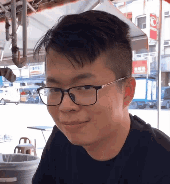 a man wearing glasses looks at the camera with a sign in the background that says ' a '