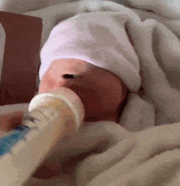 a baby in a white hat is drinking from a bottle .