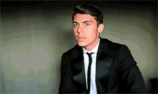a young man in a tuxedo and tie looks to his left