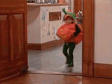 a little girl in a pumpkin costume is running out of a door .